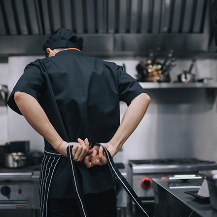 Chef cuisinier dans sa cuisine, de dos, qui attache son tablier